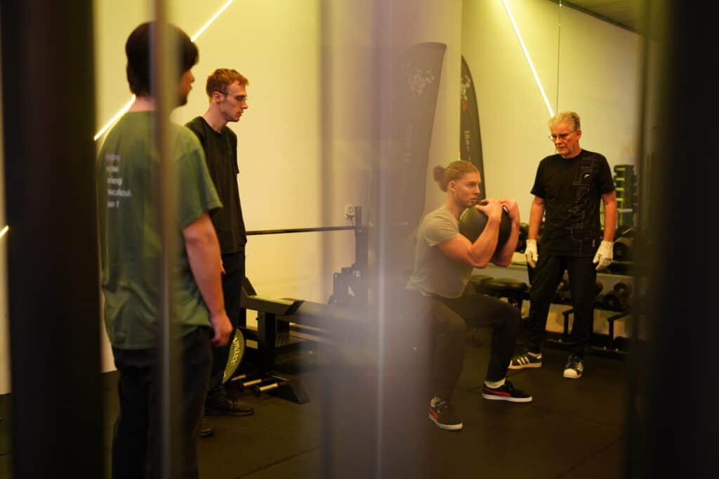 Een man doet een goblet squat met een kettlebell tijdens een begeleide training.