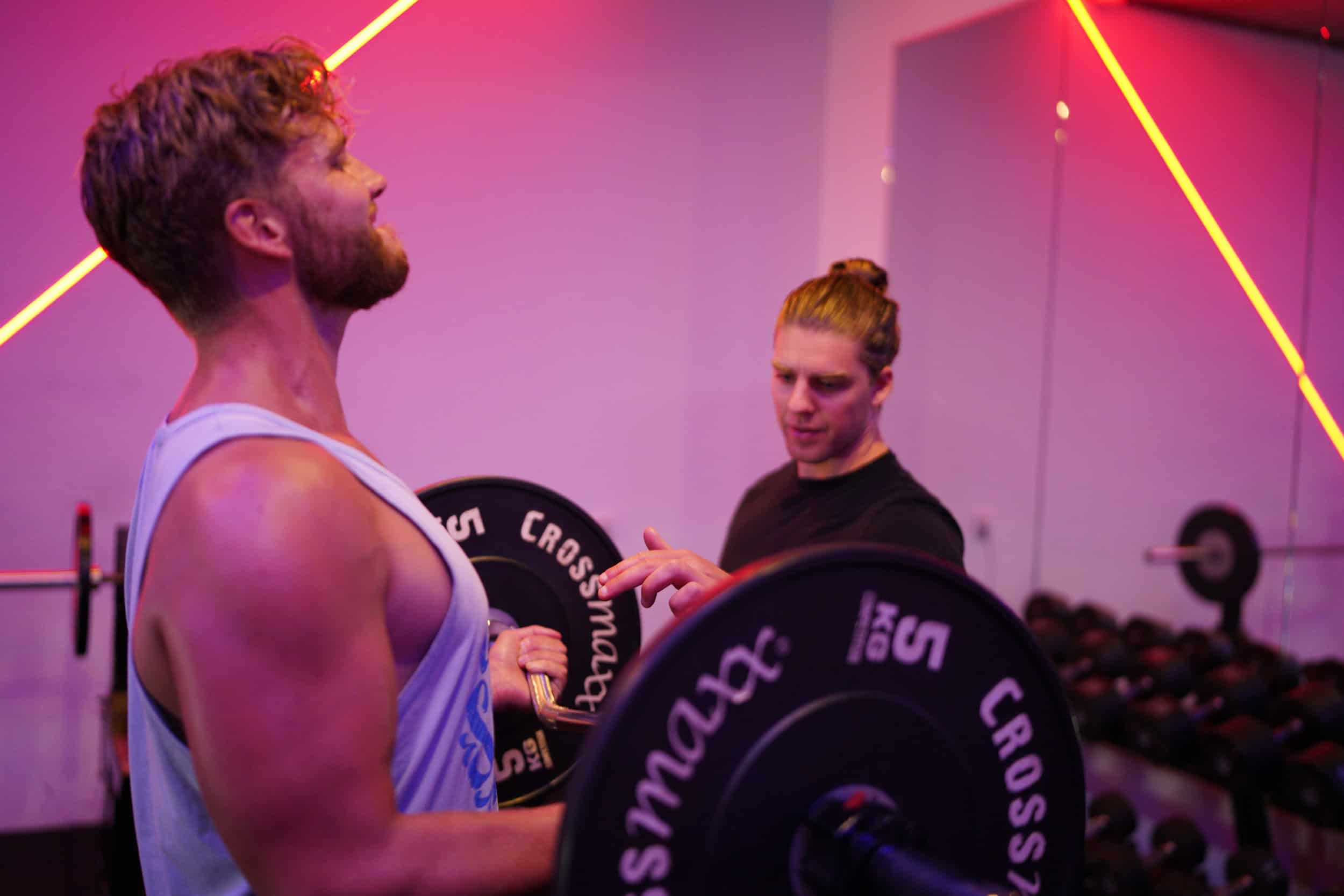 Trainer geeft een aanwijzing terwijl een man een EZ-bar curl uitvoert