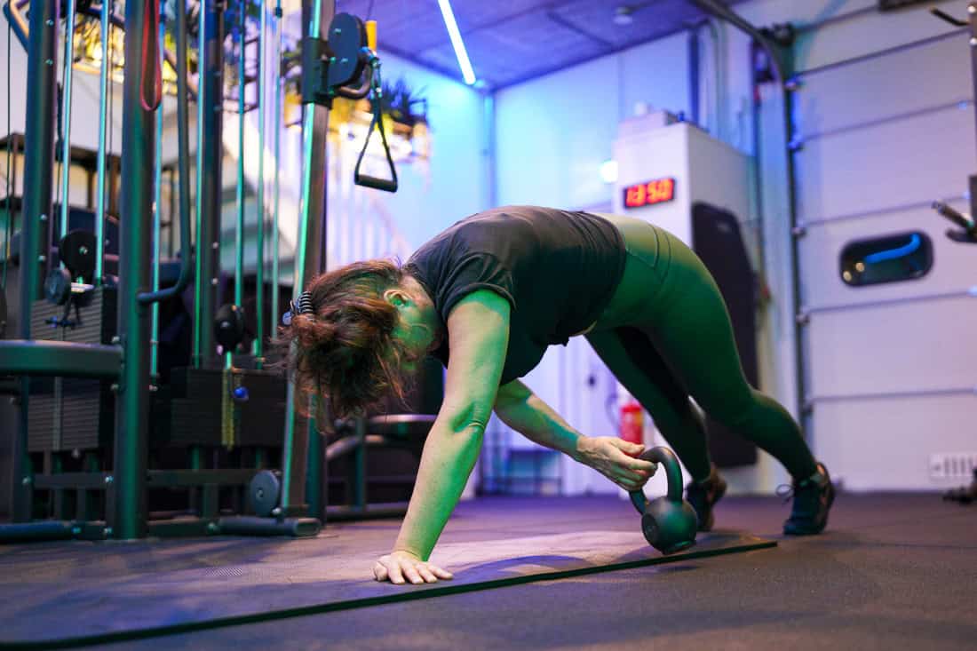 Vrouw verplaatst een kettlebell onder haar lichaam vanuit een hoge plank