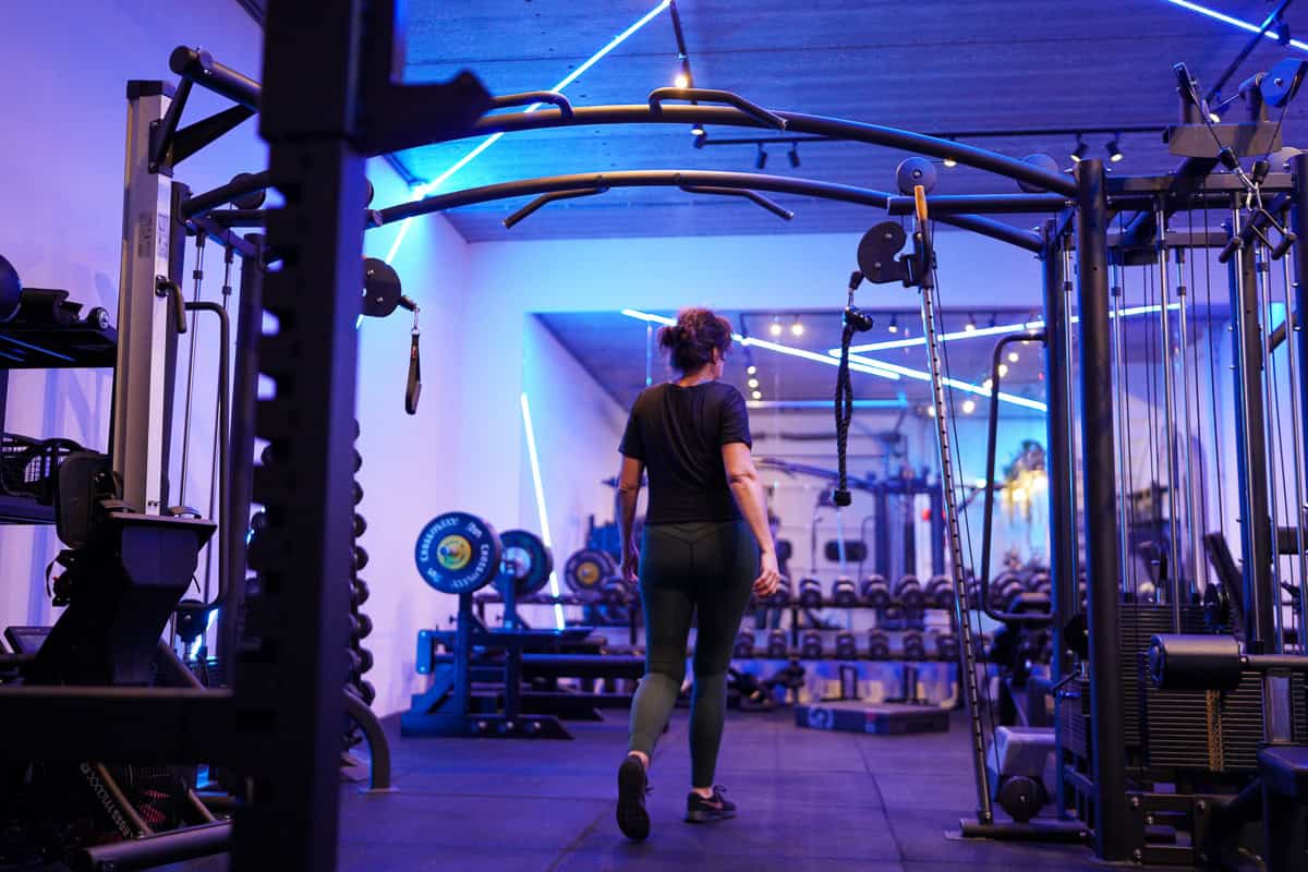 Vrouw loopt tussen de krachtapparatuur in de gym