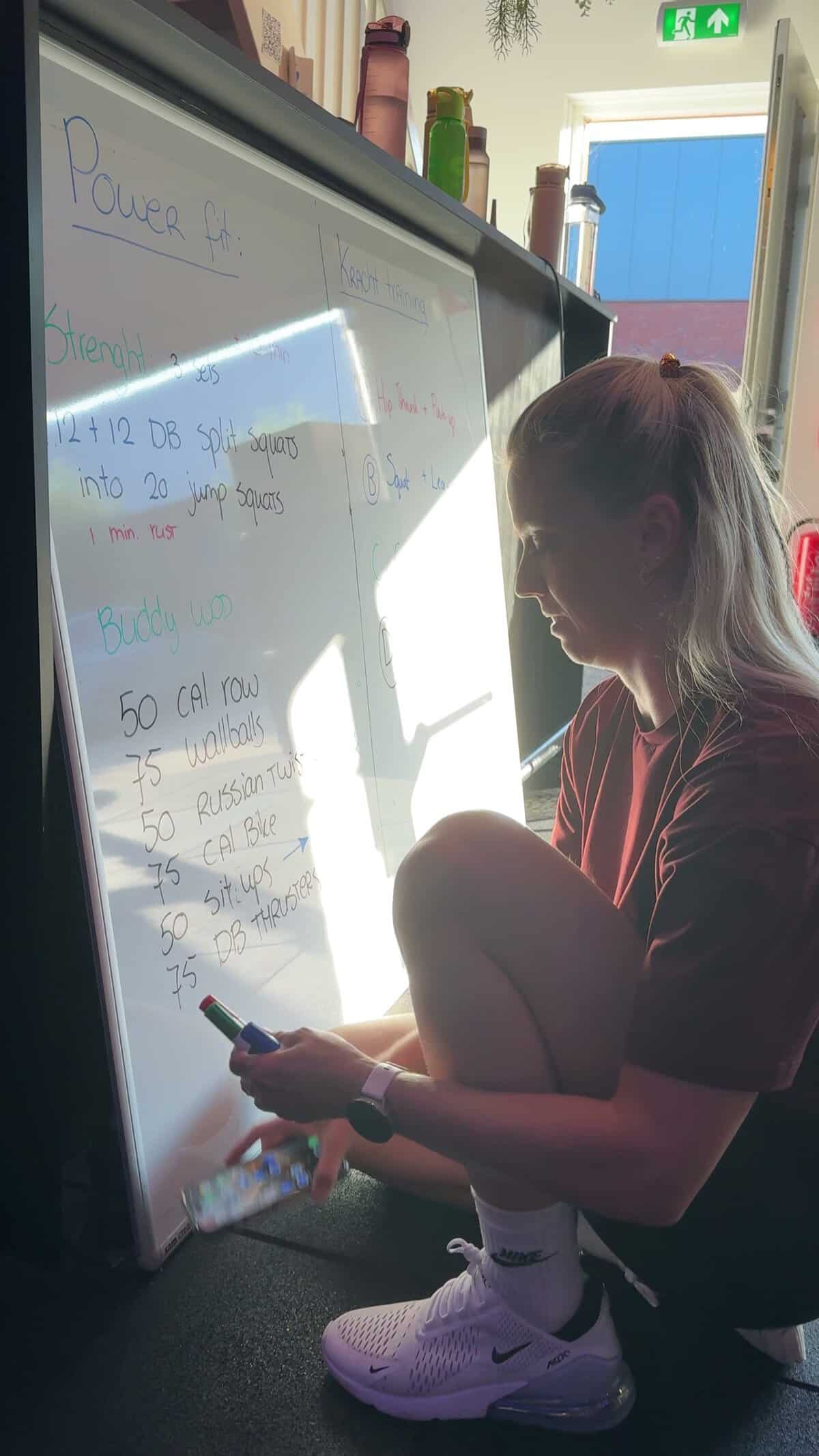Een trainer schrijft oefeningen op een whiteboard in de gym.