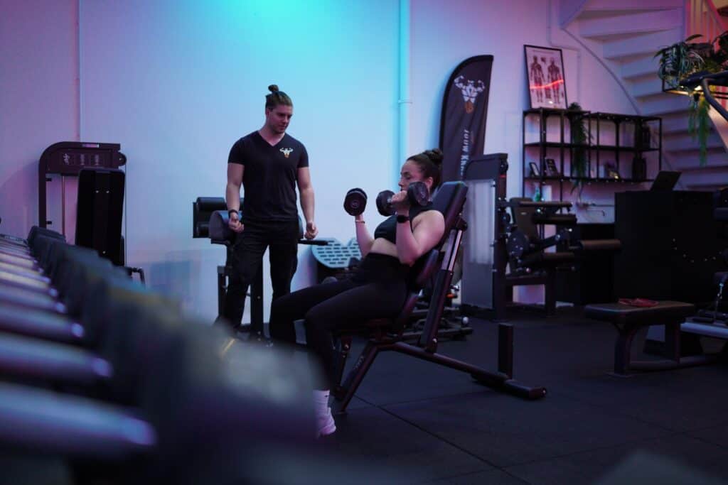 Leon begeleidt een vrouw bij dumbbell curls op een schuine bank