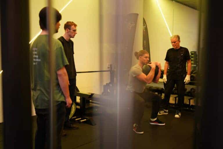 Een man doet een goblet squat met een kettlebell tijdens een begeleide training.