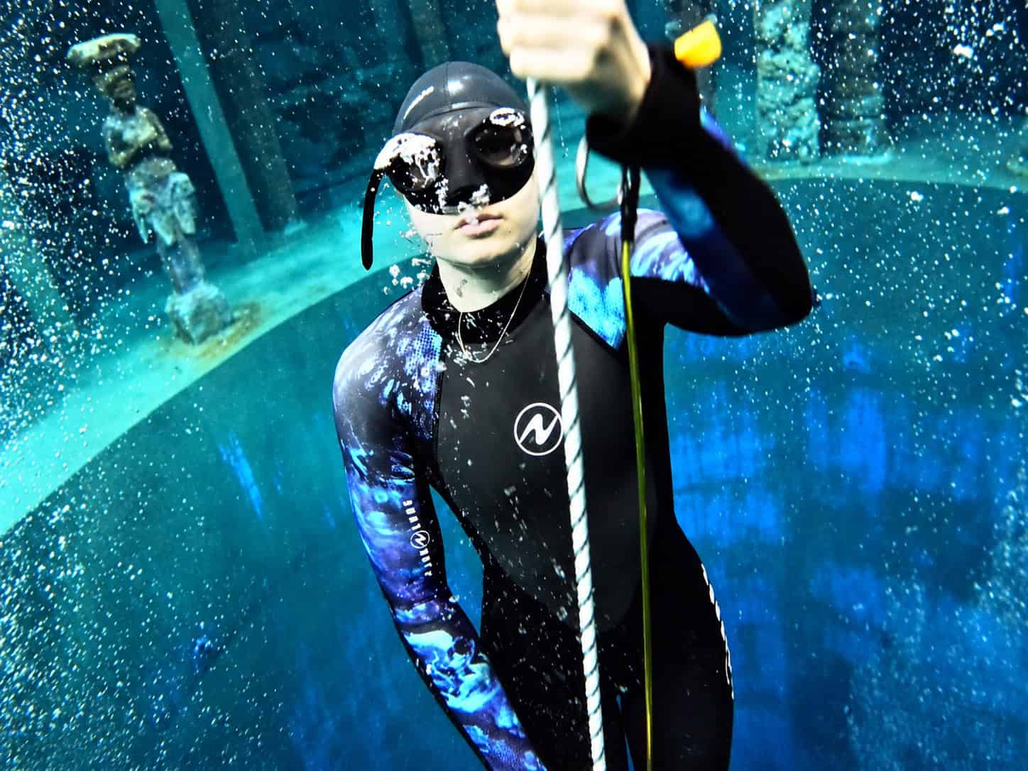 Anna tijdens het freediven, met een duikmasker en een blauw wetsuit aan de daallijn onder water.