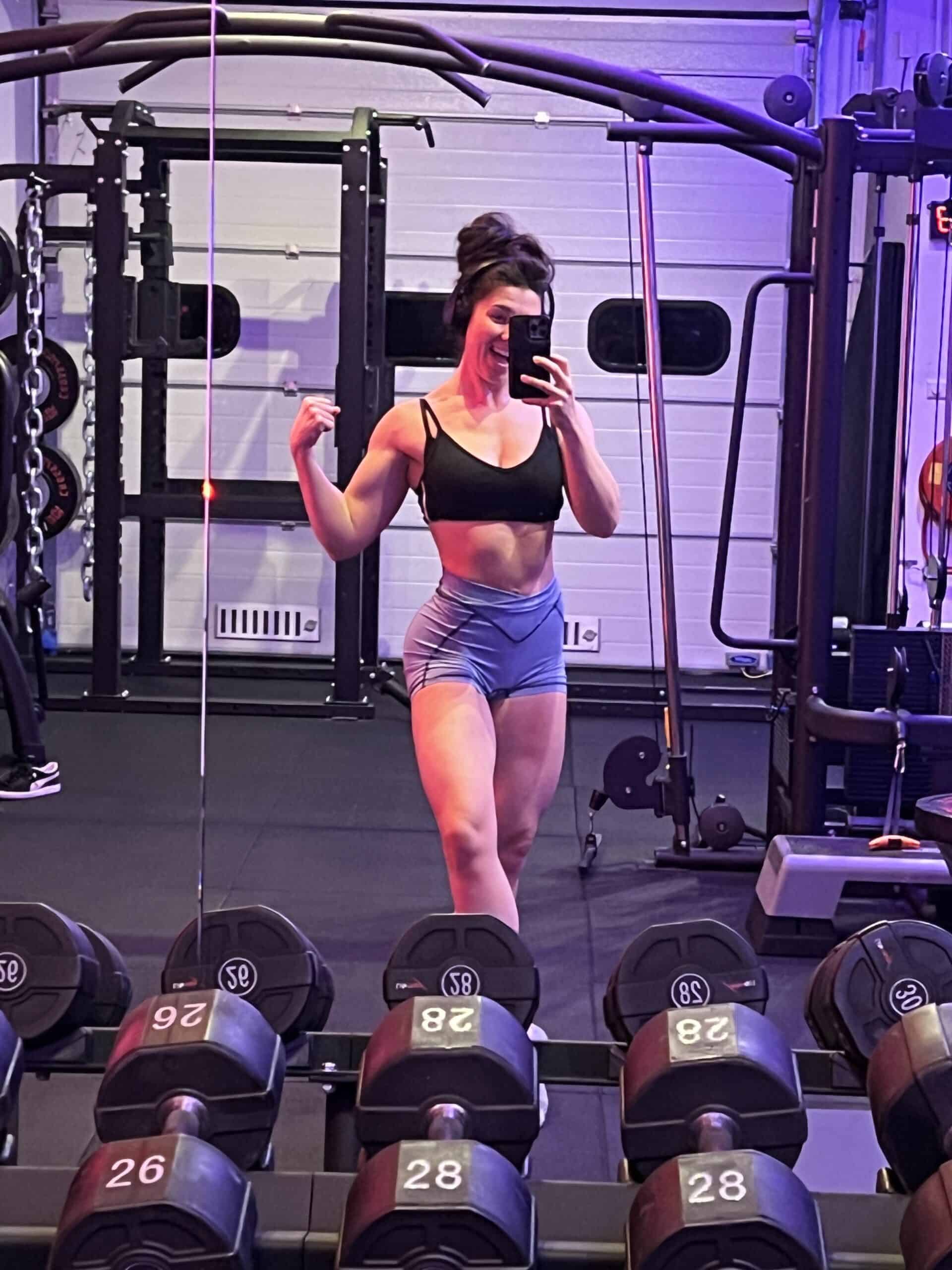 Anna maakt een spiegelselfie in de gym en spant haar arm aan.