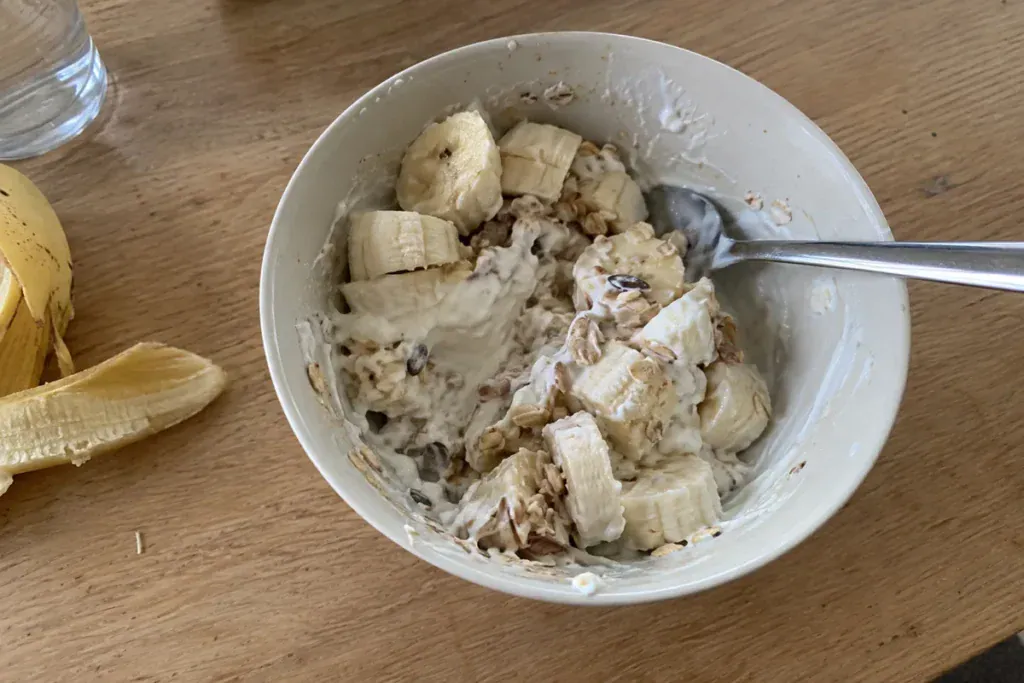Een kom kwark met banaan en muesli op een keukentafel.